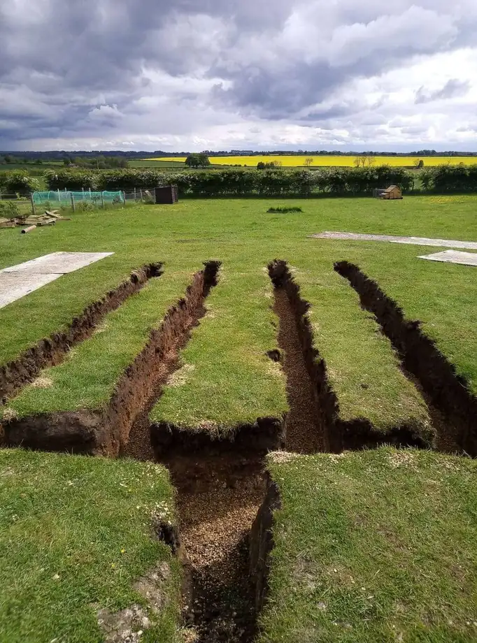 Drainage field trenches cut across a field under a heavy sky